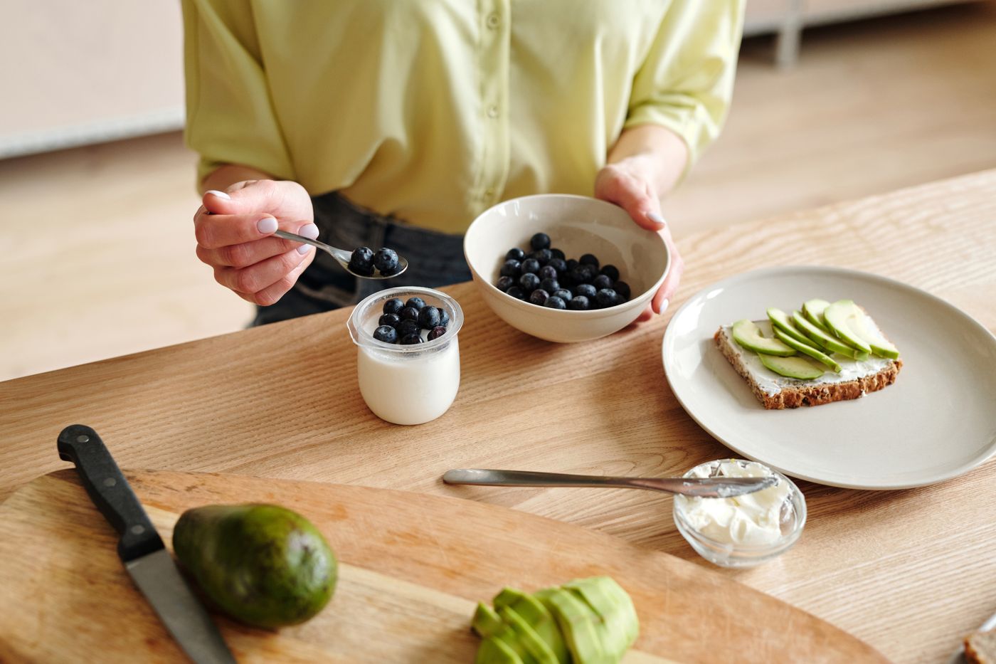 Someone adding blueberries to breakfast at a kitchen table
